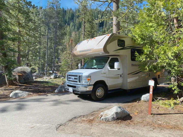 A Winnebago RV rental is parked at forest campsite 154 on a sunny day, surrounded by tall trees.. Winnebago Minnie Winnie 2019