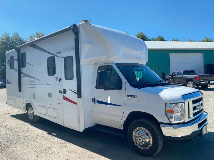 Bright white Ford E-450 Class C RV rental, parked outdoors on a sunny day against a blue sky.. Ford E450 2013