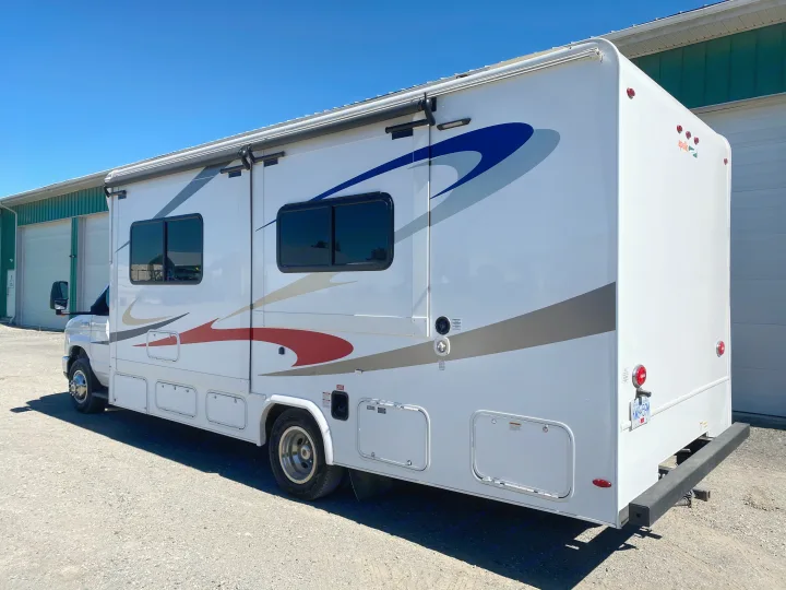 White Class C RV rental, featuring a retractable awning and multiple storage bays, under a clear blue sky.. Ford E450 2013