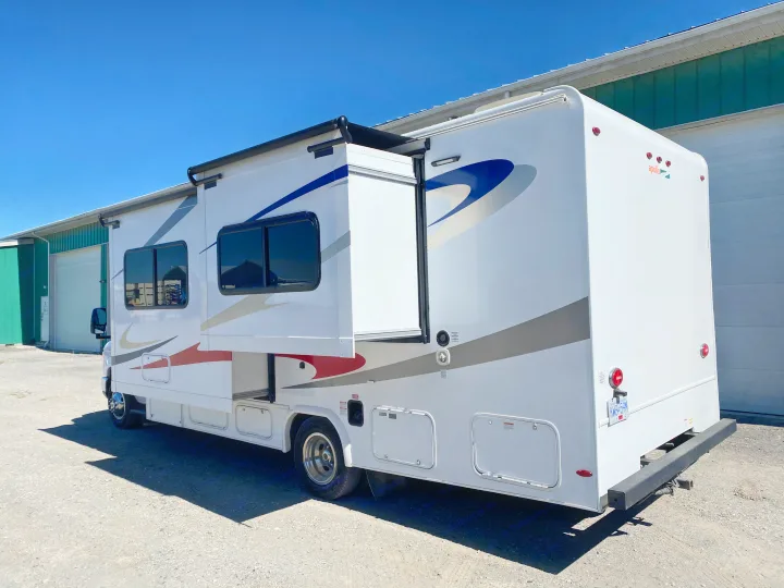 A large white Apollo RV rental with an extended slide-out, awning, and storage compartments, parked outdoors.. Ford E450 2013