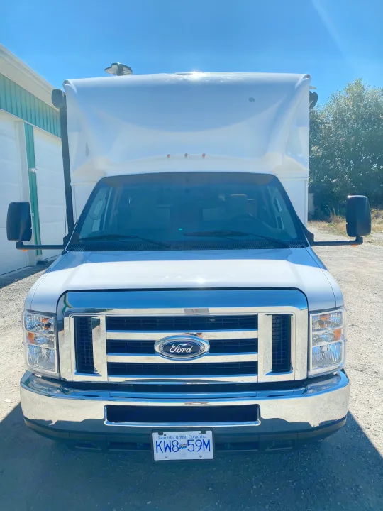Front view: A white Ford van-based RV with a large, elevated body, perfect for rv rental adventures. Parked outdoors.. Ford E450 2013