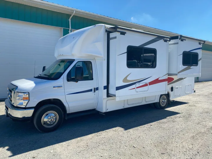 White Ford E-450 Super Duty RV rental motorhome with extended slide-outs, parked on gravel next to a green building on a sunny day.. Ford E450 2013
