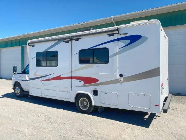 White Class C rv rental motorhome, gleaming with graphics, parked under a bright blue sky.. Ford E450 2013