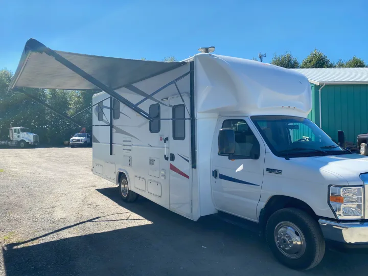 Clean white RV rental with extended awning, parked on gravel under sunny sky. Ideal for your next motorhome adventure.. Ford E450 2013