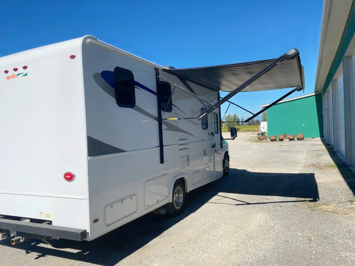 Experience an Apollo RV rental: a white Class C motorhome with an extended awning, parked on a sunny gravel lot.. Ford E450 2013