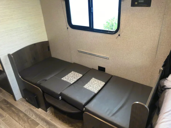 Cozy rv rental interior showcasing a dark, patterned convertible dinette/bed setup and a large window.. Jayco Jay Flight 2021