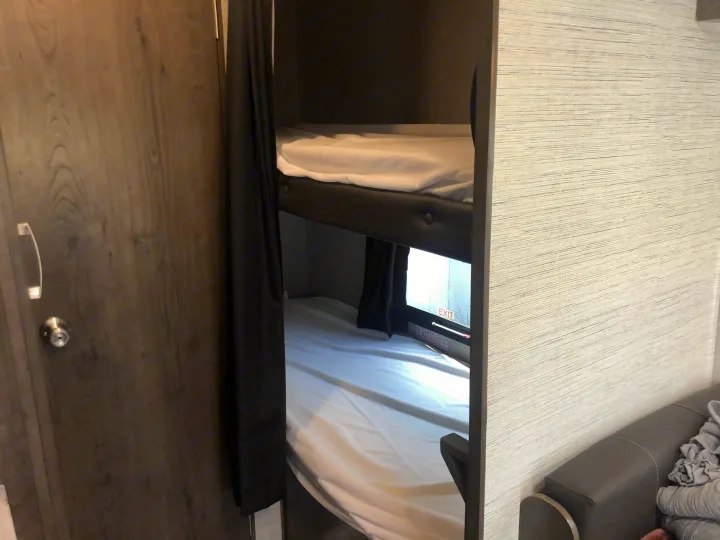 RV rental interior showcasing bunk beds with white linens and an emergency exit window, a cozy sleeping space.. Jayco Jay Flight 2021