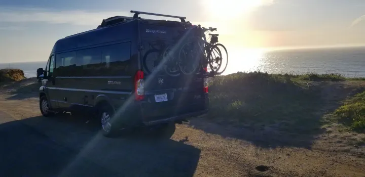 RV rental camper van with bikes parked overlooking a beautiful ocean sunset. Ideal for a scenic road trip adventure.. Thor Sequence 2021