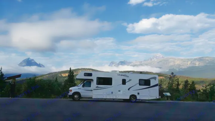 Majestic RV rental parked at a mountain scenic overlook with cloudy peaks and evergreen forests under a blue sky.. Ford Majestic 2007