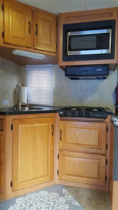 An RV rental's efficient kitchen, featuring light wood cabinets, sink, microwave, and a two-burner stovetop, perfect for mobile cooking.. Ford Majestic 2007
