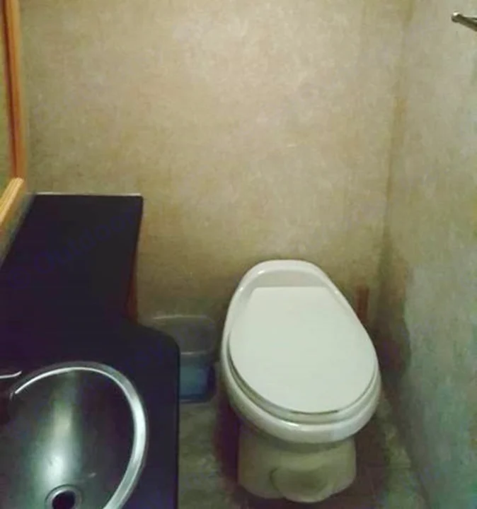Compact RV rental bathroom. A white toilet is visible on the right, and a black vanity with a metal sink is on the left.. Ford Majestic 2007