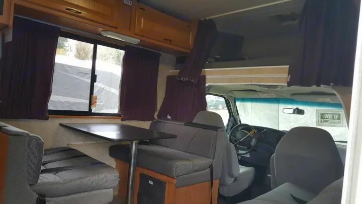 Spacious RV rental interior showcasing a dinette, overhead bunk with TV, and front cockpit, ready for travel.. Ford Majestic 2007