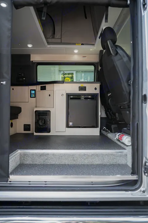 An RV rental's inviting interior: looking into a camper van with a compact kitchen, fridge, control panel, and a step up.. Ram Pleasure Way 2019