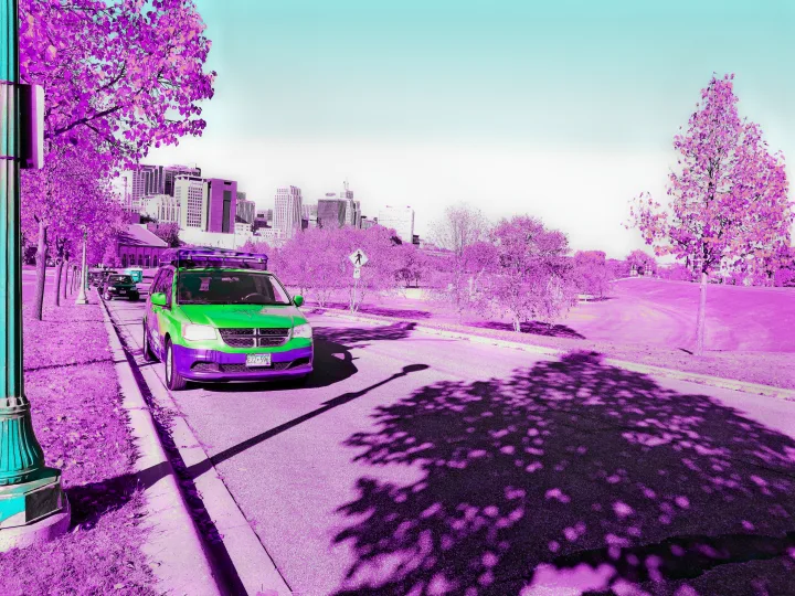 Green & purple travel van, a convenient RV rental, on a vibrant purple city street with trees and skyline.. Dodge Grand Caravan 2014