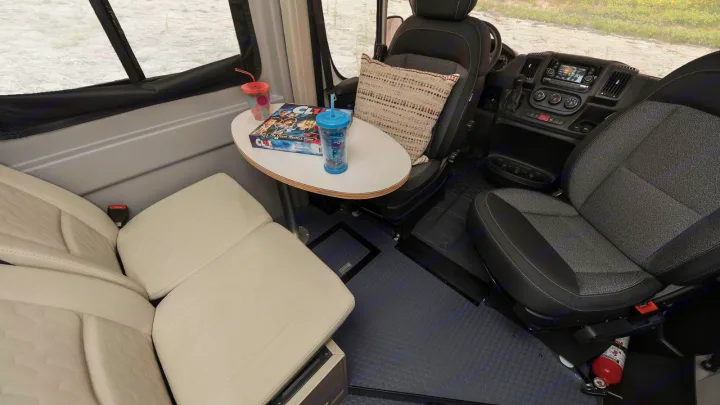 Inside an RV rental: Swivel front seats, a table with drinks & Clue, and comfy bench seating for travel.. Winnebago Solis 59PX 2021