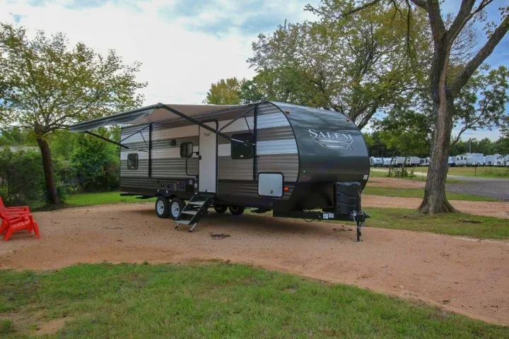 Experience camping with this spacious gray Salem travel trailer RV rental, parked on a gravel site under an extended awning, surrounded by trees.. Forest River Salem 2019