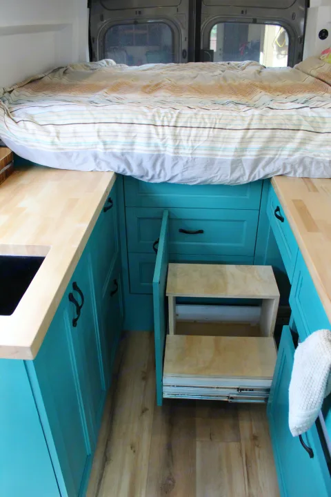 Step into comfort! This RV rental features a cozy bed, bright teal kitchen, and clever pull-out access steps.. Ford Transit 2020