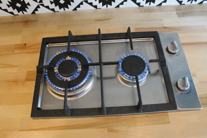 Compact two-burner gas cooktop with lit blue flames on a wood counter, perfect for your RV rental cooking adventures.. Ford Transit 2020