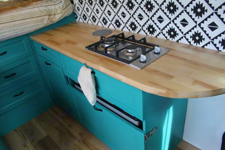 Explore this vibrant RV rental kitchen: teal cabinetry, wood countertop, gas stovetop, and graphic backsplash.. Ford Transit 2020