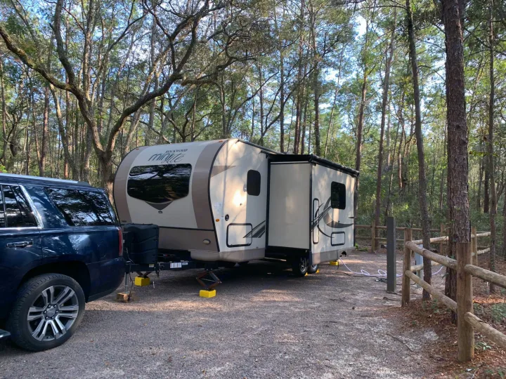 An RV rental travel trailer is parked on a gravel campsite amidst tall trees.. Other Other 2019