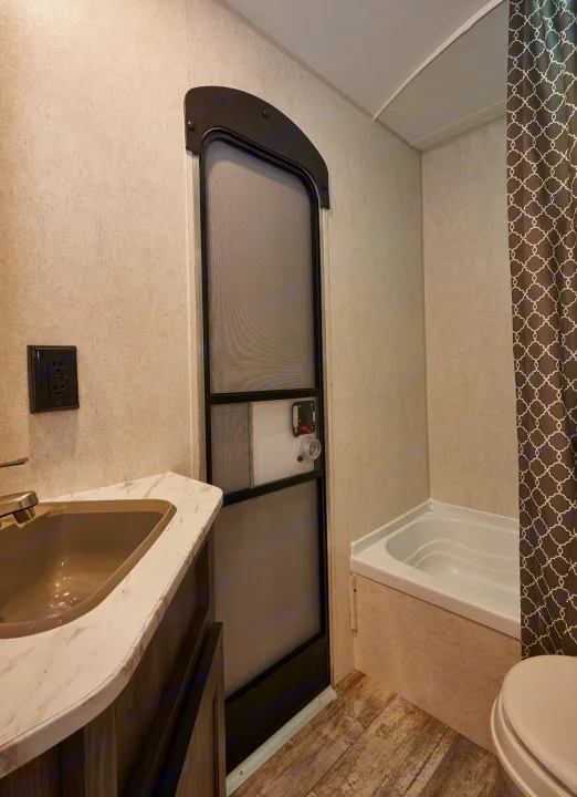 This RV rental bathroom features a compact sink, bathtub, and screen door, ideal for travel comfort.. Open Range Open Range 2020
