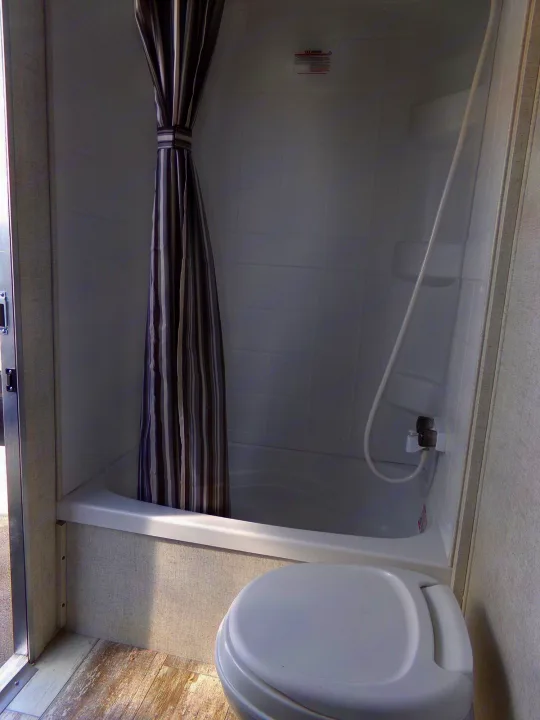 RV rental bathroom: A compact space featuring a tub/shower with a striped curtain and a white toilet.. Open Range Open Range 2020