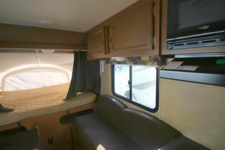 An RV rental interior with a cozy pop-out bed on the left, a sofa on the right, and overhead cabinets.. Starcraft Launch 2014