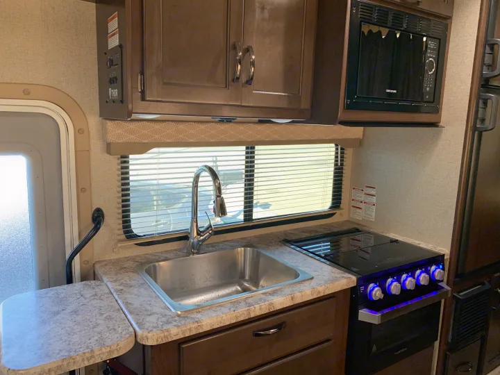 RV rental interior features a compact kitchen with a sink, gas cooktop, microwave, and ample storage cabinets.. Thor Freedom Elite 2021