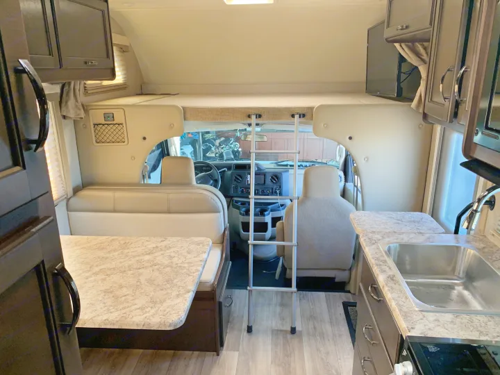 RV rental interior: kitchen, dinette, overhead bunk with ladder. Bright and spacious living area for travel.. Thor Freedom Elite 2021