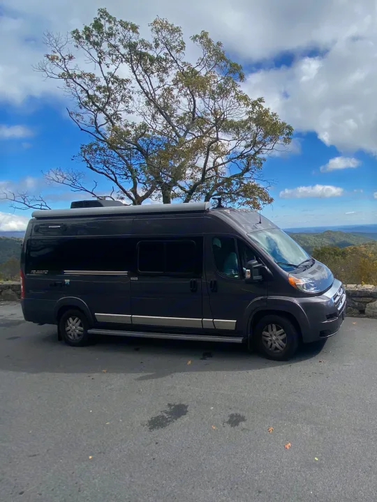 Experience freedom with an RV rental! This dark gray camper van enjoys a stunning mountain overlook view under a beautiful sky.. Winnebago Travato 2018