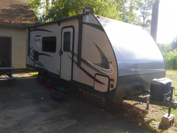 Grey Coleman RV rental travel trailer parked outdoors on a sunny day beside a building.. Coleman Other 2018