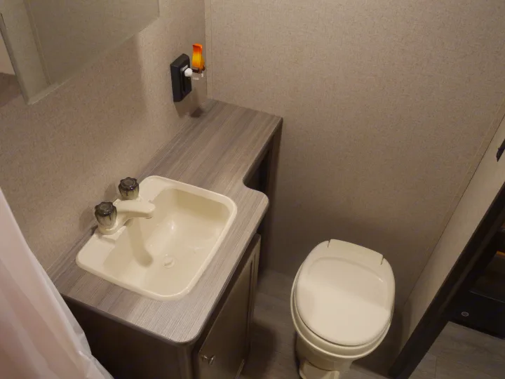 Compact RV rental bathroom. Features a light sink, two-handle faucet, toilet, and textured walls, designed for travel comfort.. Coleman Other 2018
