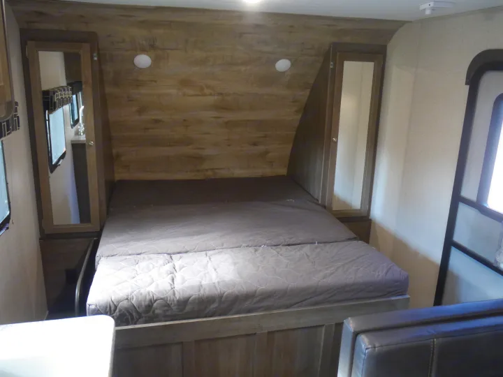 This RV rental bedroom features a comfortable queen bed, wood-paneled walls, and mirrored wardrobes.. Coleman Other 2018