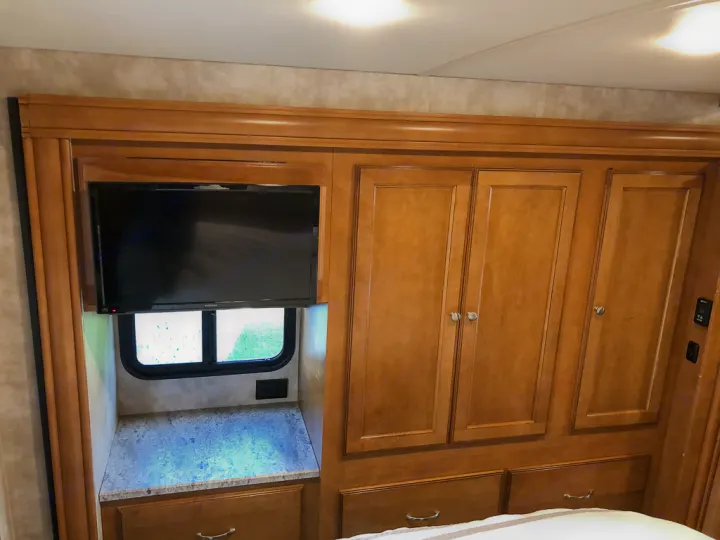 Explore this RV rental bedroom: built-in wood cabinetry, TV, window nook, and storage drawers. A comfortable stay awaits.. Winnebago Vista 2018