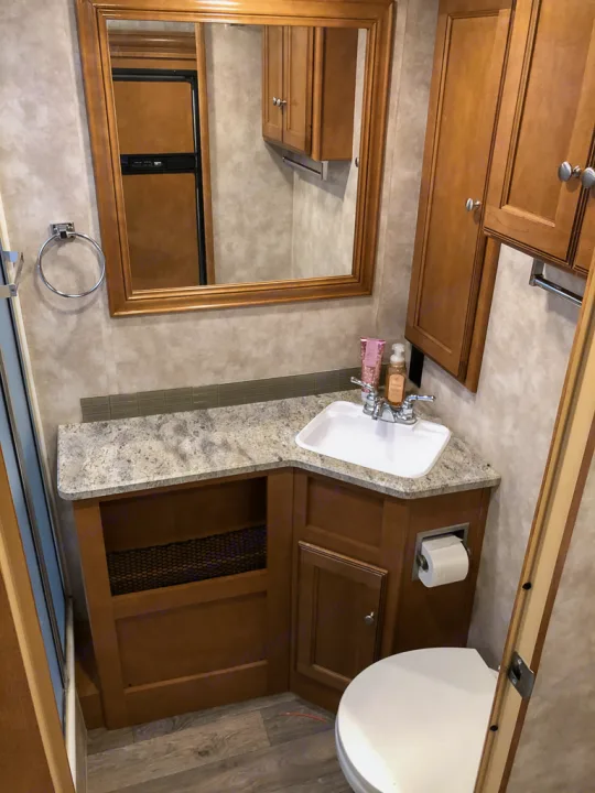 RV rental bathroom: compact vanity, sink, toilet, mirror reflects kitchen. Efficient interior design with storage.. Winnebago Vista 2018
