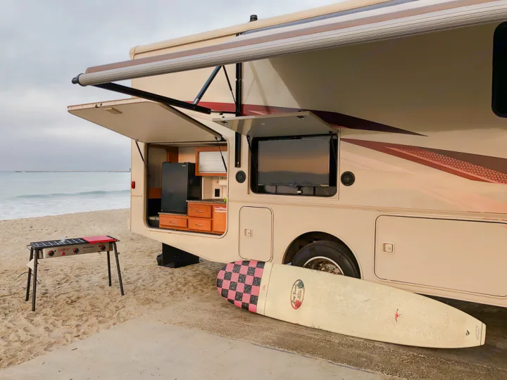 Beach day setup: This RV rental features an outdoor kitchen, TV, grill, and surfboard, perfect for oceanfront adventure.. Winnebago Vista 2018