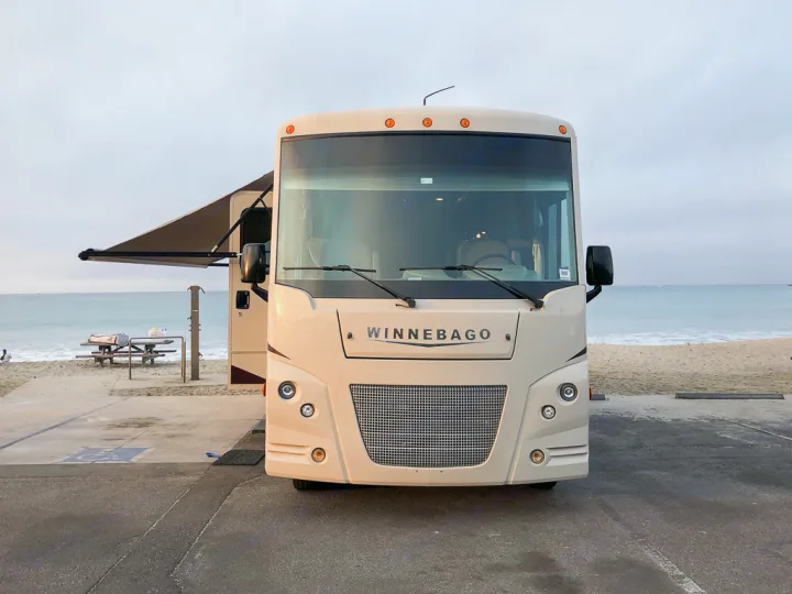 Winnebago RV rental parked oceanside on a sandy beach. Perfect for coastal camping and travel adventures.. Winnebago Vista 2018