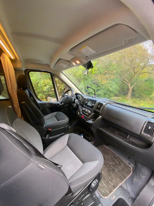 Inside an RV rental: spacious front cab with seats, dashboard, and steering wheel, ready for adventure.. Winnebago Travato 2018