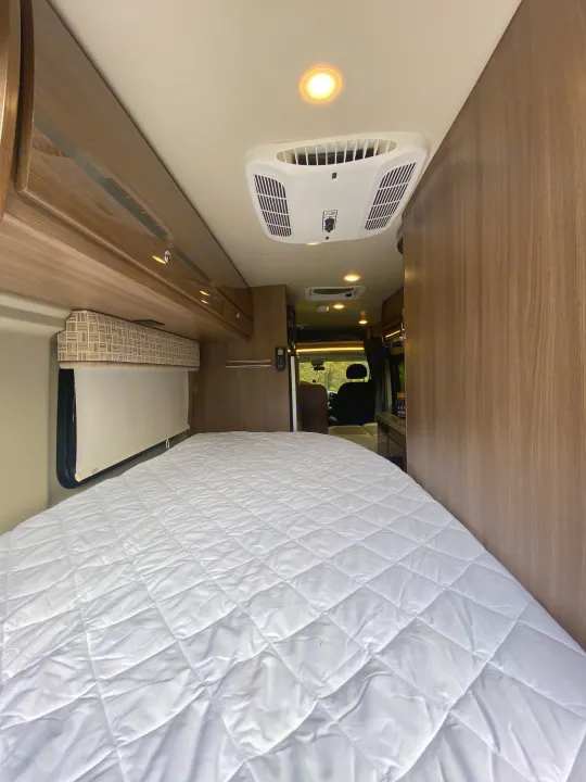 Comfortable bedroom in an RV rental, featuring a quilted mattress, overhead storage, and ceiling AC. Ready for travel!. Winnebago Travato 2018
