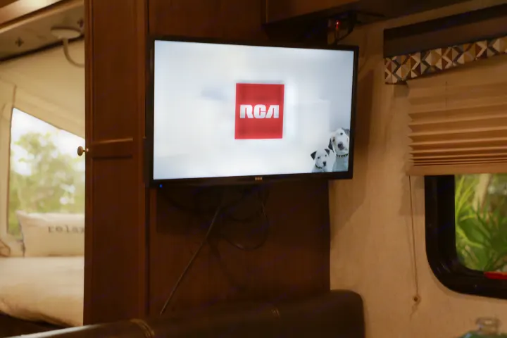 Inside an RV rental: a TV shows the RCA logo and dogs. A bed with a "relax" pillow and window with blinds are also visible.. Starcraft Other 2018