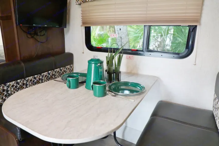 Inside an RV rental: a cozy dinette with green dishes, TV, and window showing palm trees.. Starcraft Other 2018