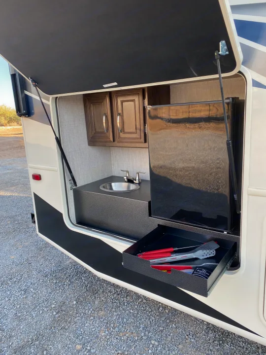 RV rental outdoor kitchen: sink, fridge, cabinets, and a pull-out drawer with BBQ tools. Perfect for camping trips!. Entegra Coach Other 2021