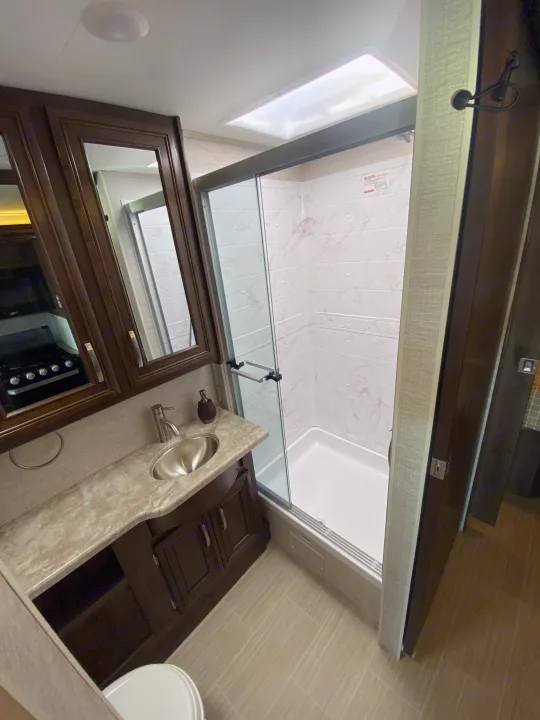 Modern RV rental bathroom with a vanity, sink, mirrored cabinets, a walk-in shower with glass doors, and a toilet.. Entegra Coach Other 2021