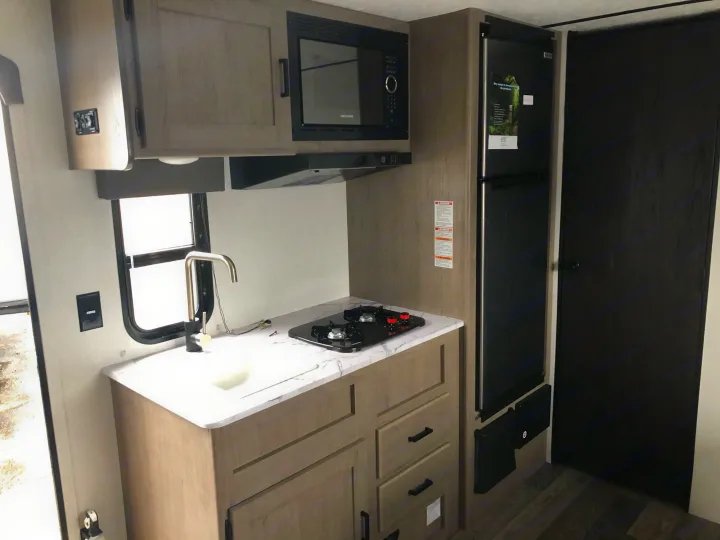 Compact RV rental kitchen featuring a sink, two-burner stovetop, microwave, and refrigerator for convenient travel.. Keystone Hideout 179LHS 2021