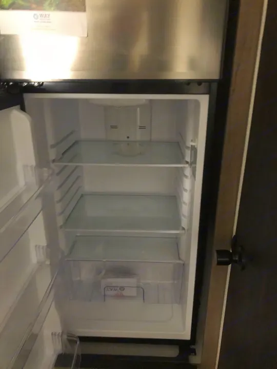 Empty, clean RV rental refrigerator with glass shelves and a top freezer, ready for your journey.. Keystone Hideout 179LHS 2021