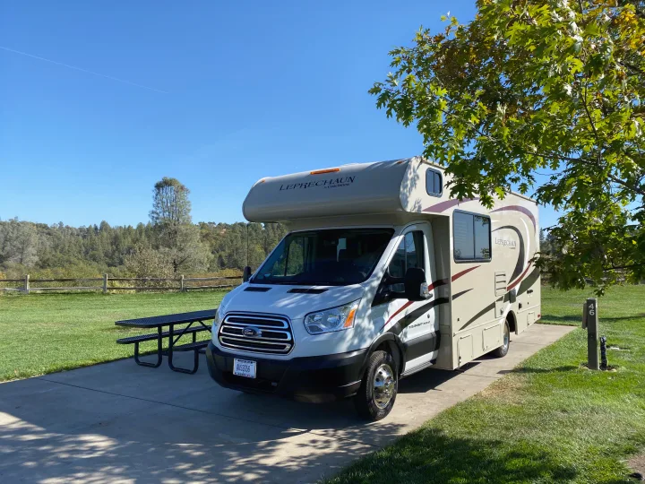 White Class C RV rental parked on a concrete pad in a sunny campground, next to a picnic table and green grass.. Other Other 2020