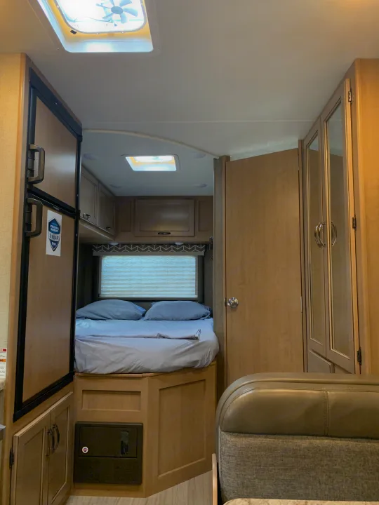 Cozy RV rental interior featuring a light blue bed, refrigerator, and wooden cabinetry with a ceiling vent.. Thor Daybreak 2020