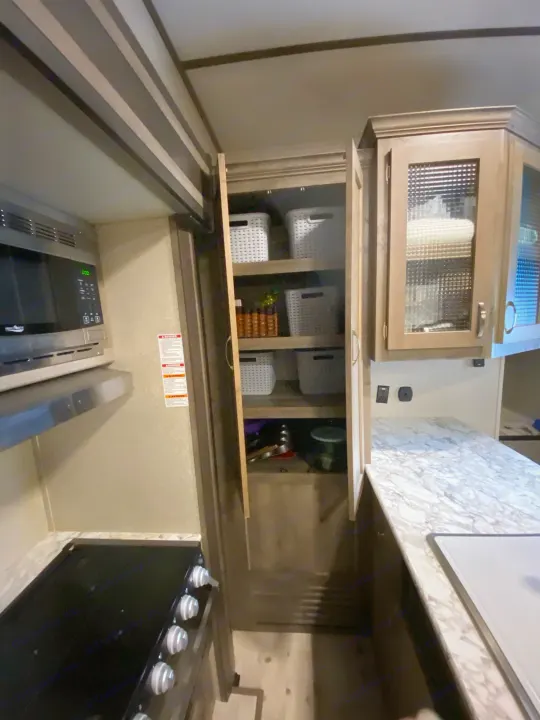 This RV rental kitchen boasts a microwave, stove, marbled counter, and an organized pantry with baskets for convenience.. Keystone RV Sprinter Campfire Edition 2020