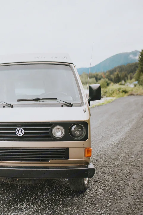 Front 3/4 view of a beige VW Westfalia camper van on a gravel road, ready for rv rental adventures.. Volkswagen syncro 1986