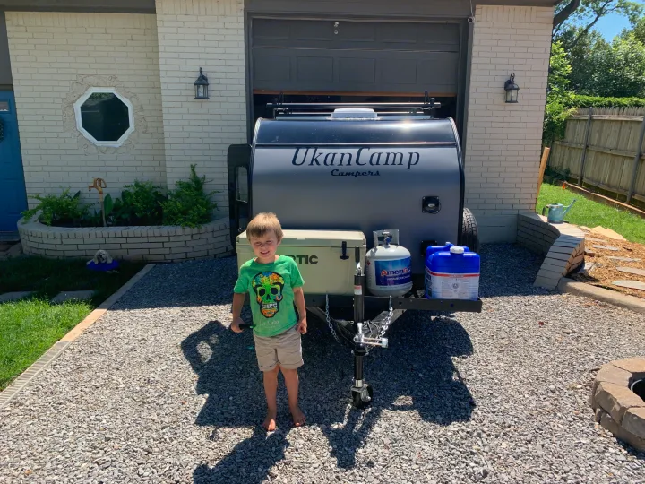 A happy boy stands proudly in front of a small UkanCamp travel trailer, ideal for an RV rental adventure.. Little Guy Other 2020